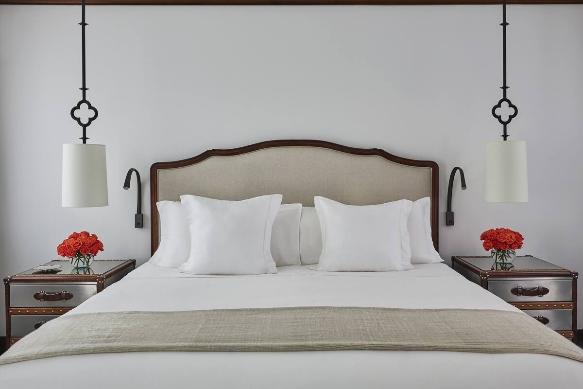 Un lit bien fait, avec du linge de lit blanc et deux tables de chevet ornées de roses rouges.