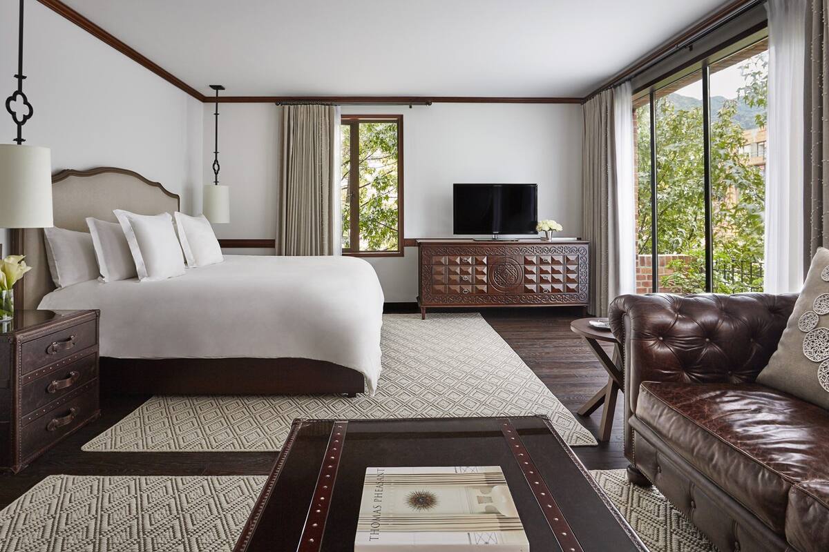 Une chambre d’hôtel avec un grand lit, une télévision, un canapé en cuir et une vue sur la verdure.