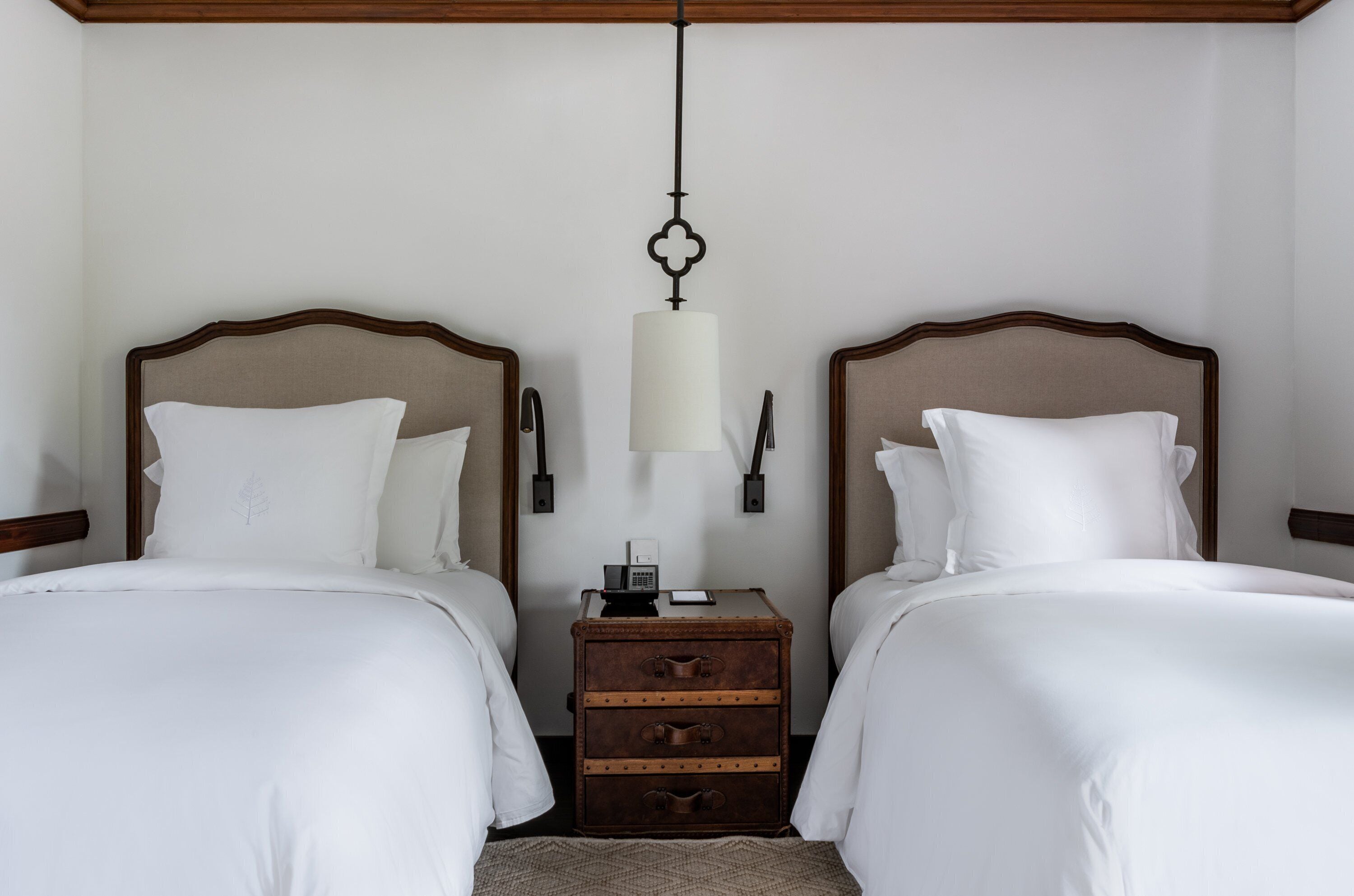 A hotel room with two beds, a nightstand, and a lamp.