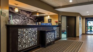 A reception area with a modern design, featuring a large digital display, a seating area with a patterned backrest, and a reception desk with a glass panel.
