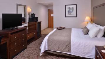 Quarto de hotel com cama, escrivaninha com televisão, cômoda e um quadro na parede.