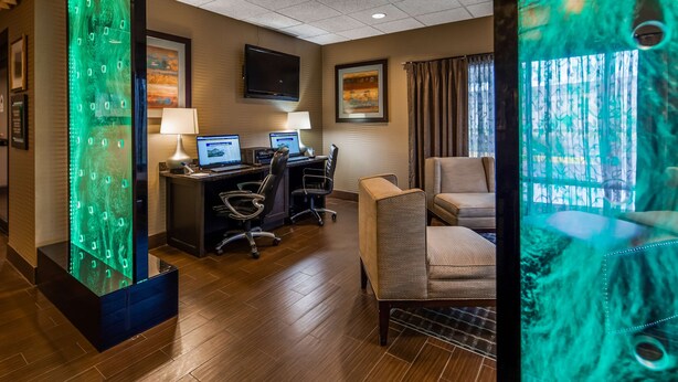 A hotel room with a wooden floor, two desks with computers, a sofa, and a large window with curtains.