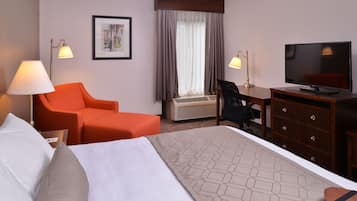 Ett hotellrum med en säng, ett skrivbord, en stol, en tv och ett fönster med gardiner.