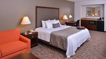 A hotel room with a bed, two bedside tables with lamps, a desk with a chair, and a kitchenette area.