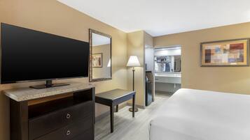Habitación de hotel con cama, televisor, escritorio, lámpara, espejo y baño a la vista.