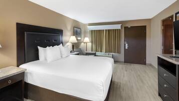 A hotel room with a large bed, bedside tables, a desk, a chair, a television, and a door.