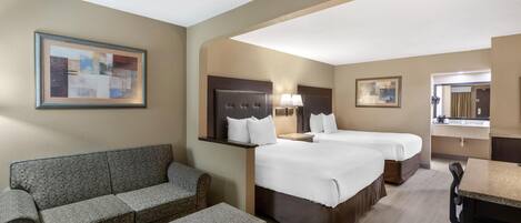 A hotel room with two beds, a sofa, a desk, and a bathroom visible in the background.