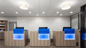 Zona de recepción con tres mostradores de madera, cada uno con un panel azul iluminado. La zona presenta una pared de ladrillo blanco e iluminación empotrada en el techo.