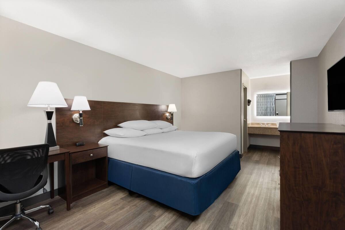 Een hotelkamer met een bed, bureau, stoel, lampen en een televisie.
