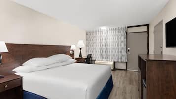 Een hotelkamer met een groot bed, nachtkastjes met lampen, een bureau, een stoel, een televisie en een kledingkast.