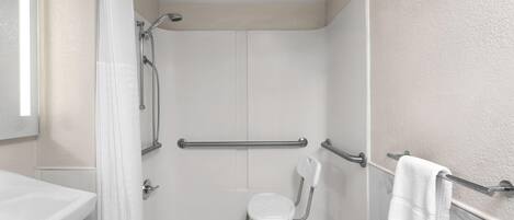 Une salle de bain avec une douche, des toilettes et un lavabo. On y trouve une chaise blanche et un porte-serviettes.