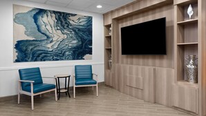 Una habitación con una televisión grande de pared, dos sillas azules, una mesita y una obra de arte de mármol.