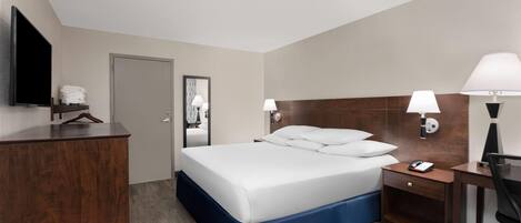 A hotel room with a bed, a desk, a chair, a TV, and a door.
