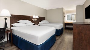 Habitación de hotel con dos camas, un escritorio, una silla, un televisor y un baño a la vista.