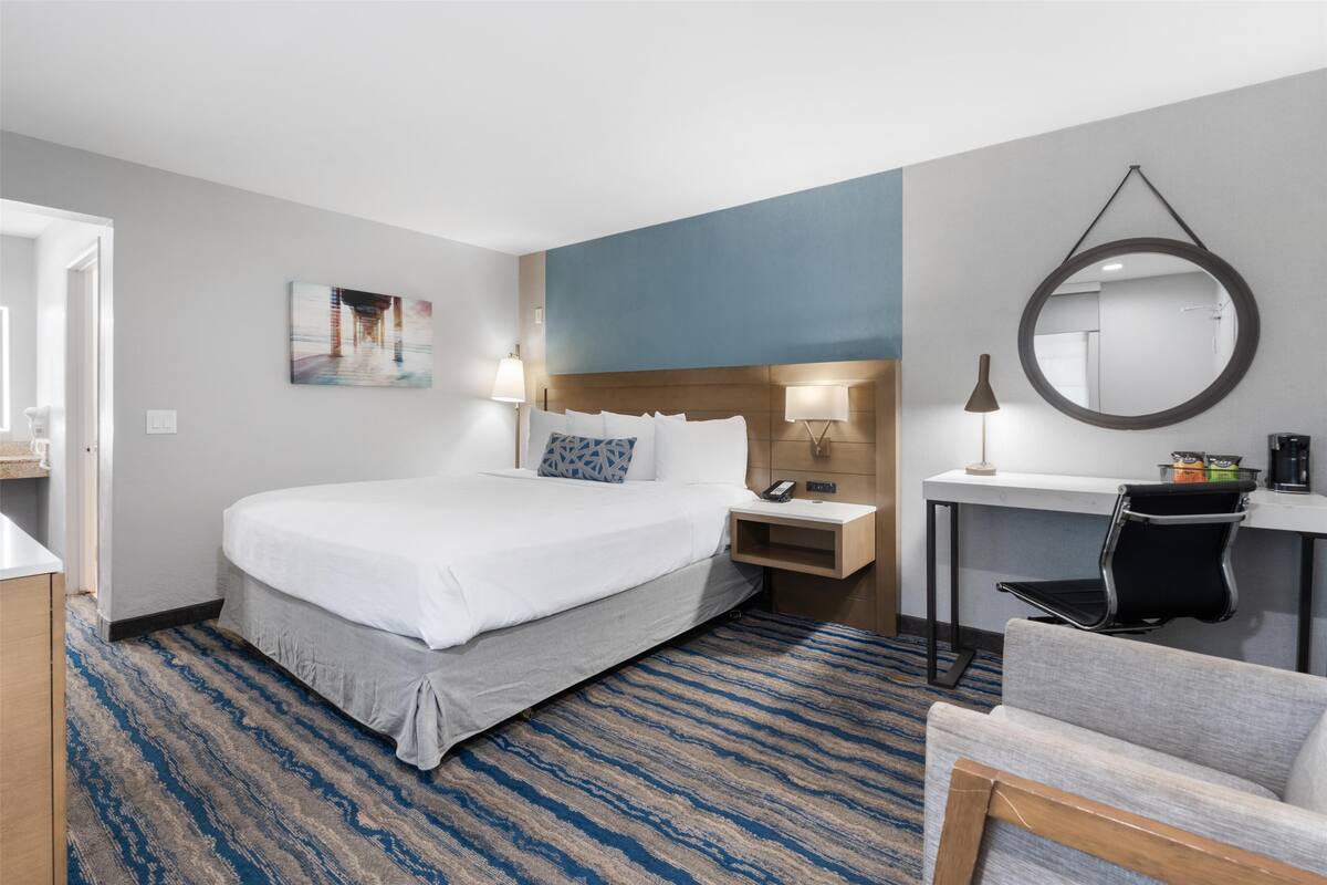 Een hotelkamer met een groot bed, een bureau, een stoel, een ronde spiegel en een schilderij aan de muur.