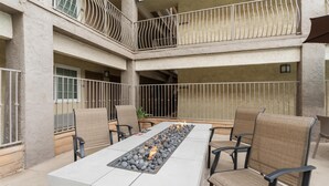 Un amplio patio al aire libre con una larga mesa rectangular, varias sillas y una chimenea integrada.