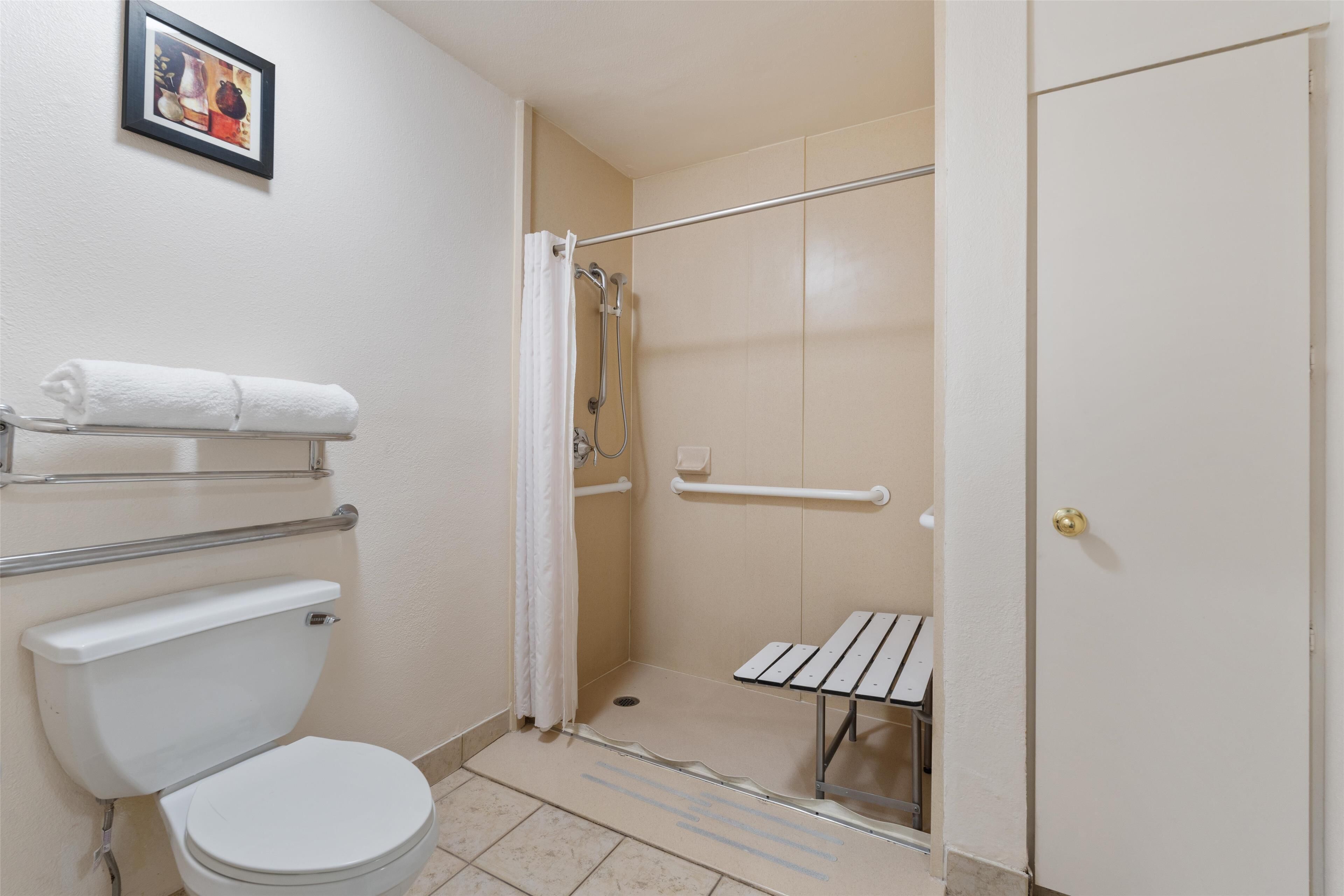 Un baño con inodoro, ducha con puerta de cristal, toallero y una puerta con manija.