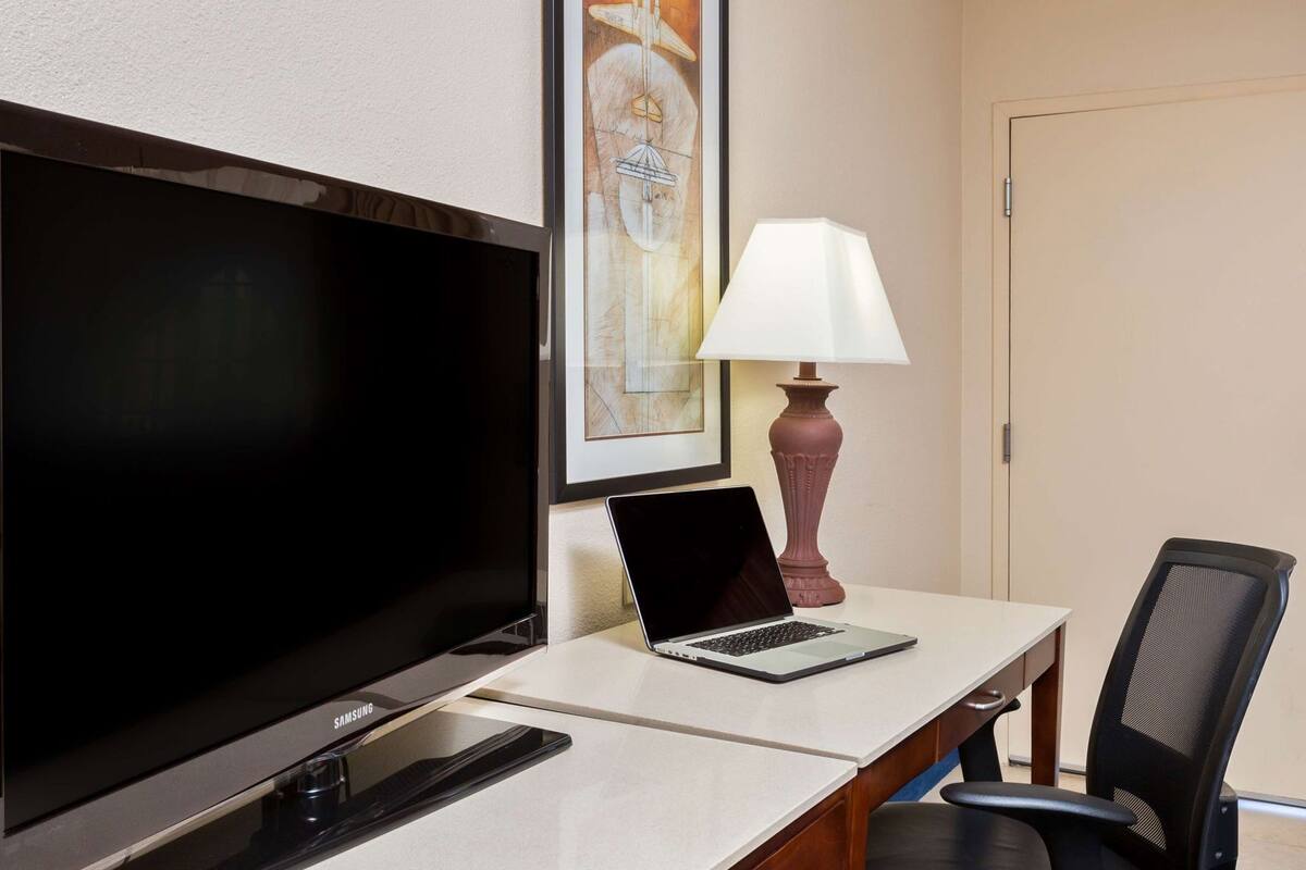 Een hotelkamer met een flatscreen televisie, een laptop op een bureau, een lamp en een stoel.
