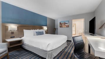 A hotel room with a large bed, a desk, a chair, a TV, and a painting on the wall.
