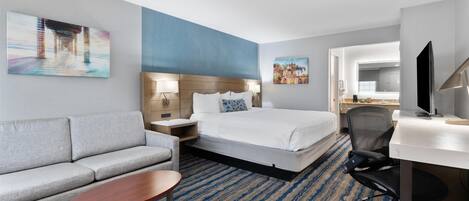 A hotel room with a bed, a sofa, a desk, and a TV.