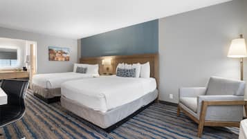 A hotel room with two beds, a desk, a chair, a lamp, and a painting on the wall.