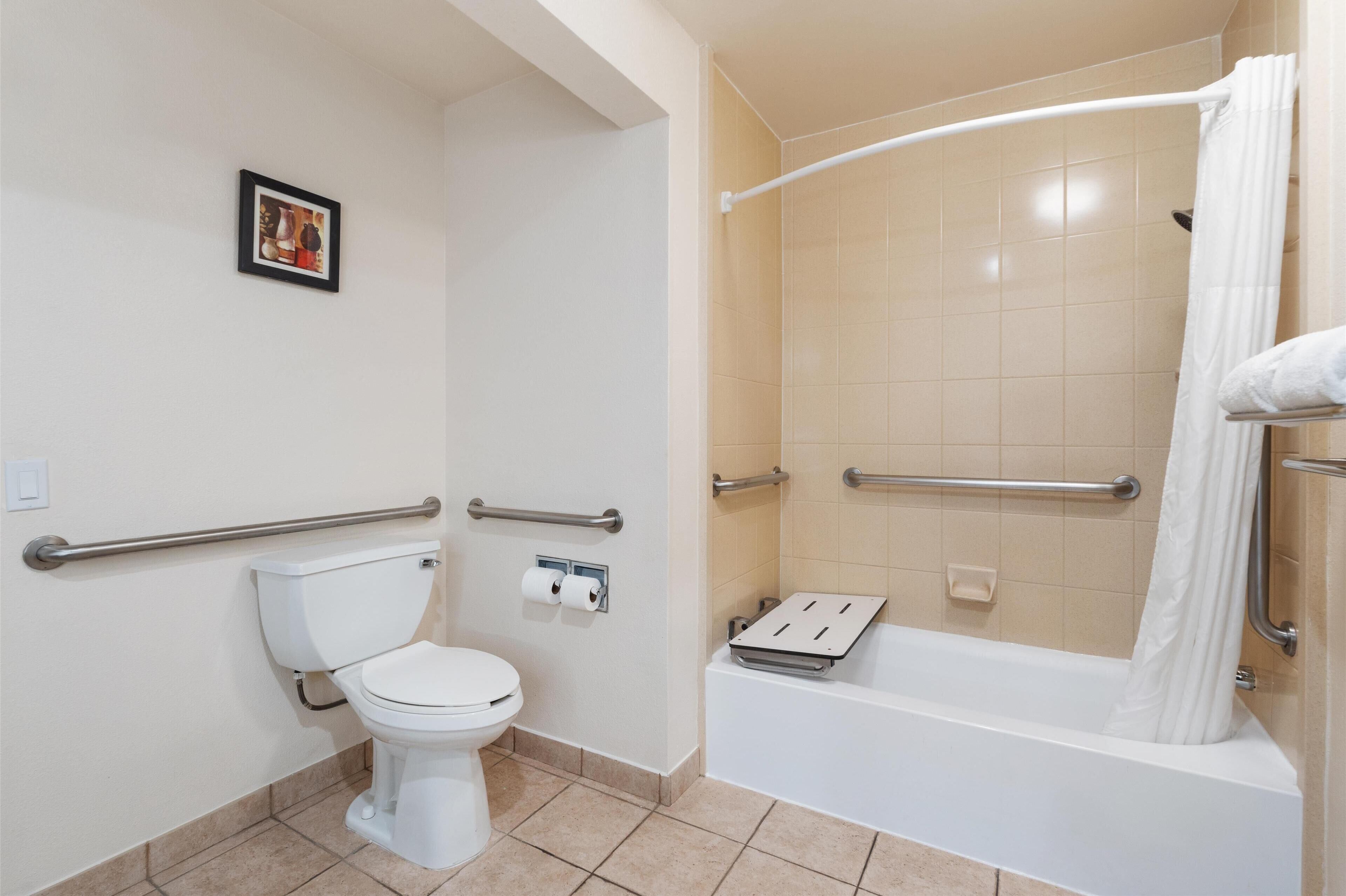A bathroom with a toilet, a shower with a grab bar, and a towel rack.