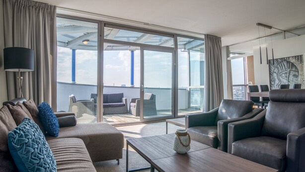 A modern hotel room with a large sliding glass door leading to a balcony, a sofa, a coffee table, and a chair. - Bilderberg Parkhotel Rotterdam (Rotterdam)
