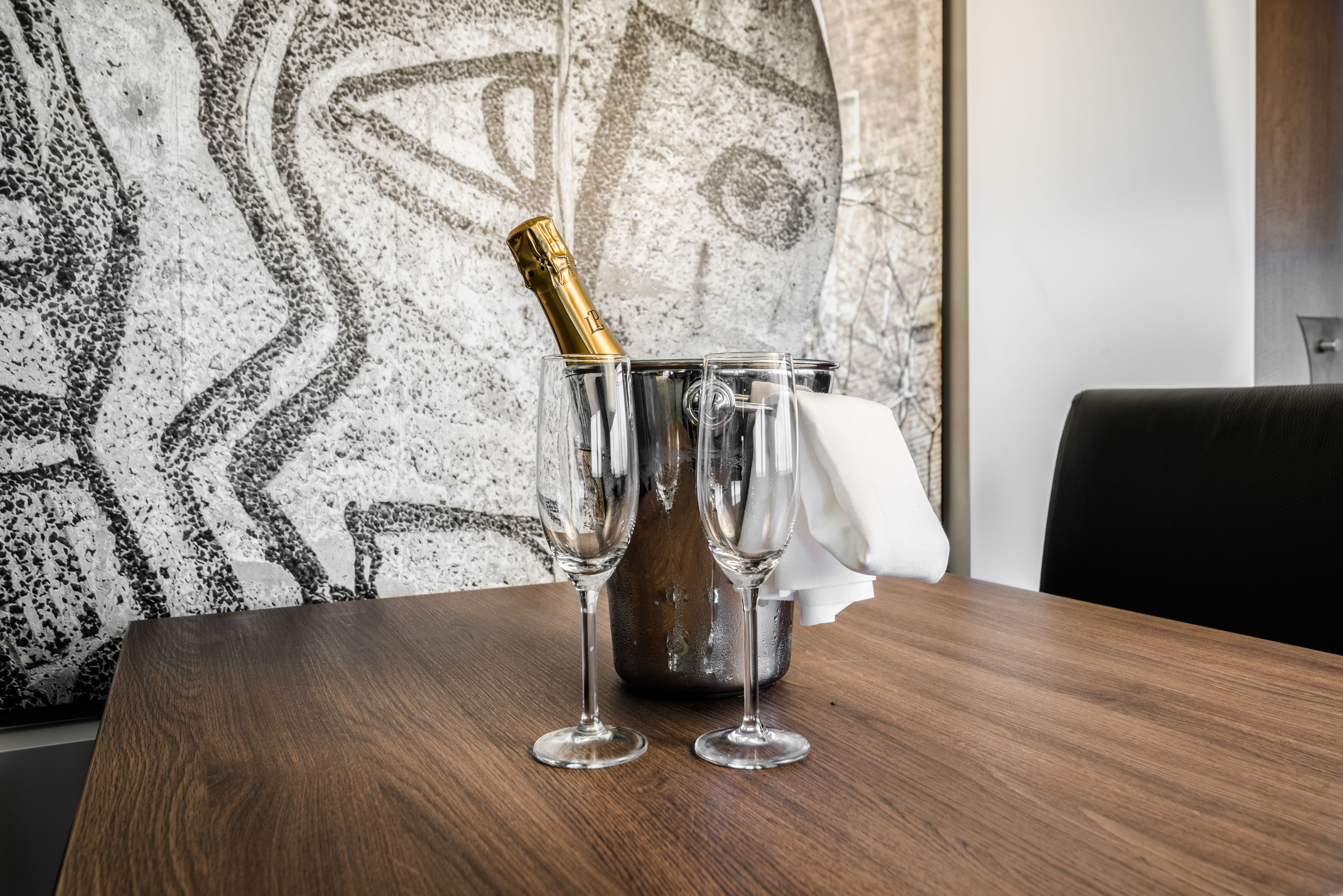 A wooden table with two empty champagne flutes and a bottle of champagne in a metal bucket.