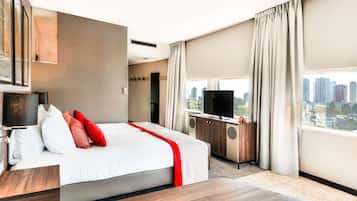 Ein modernes Hotelzimmer mit einem großen Bett, einem Flachbildfernseher, einem Schreibtisch und Blick auf die Stadt.
