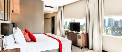 A modern hotel room with a large bed, a flat-screen TV, a desk, and a city view.