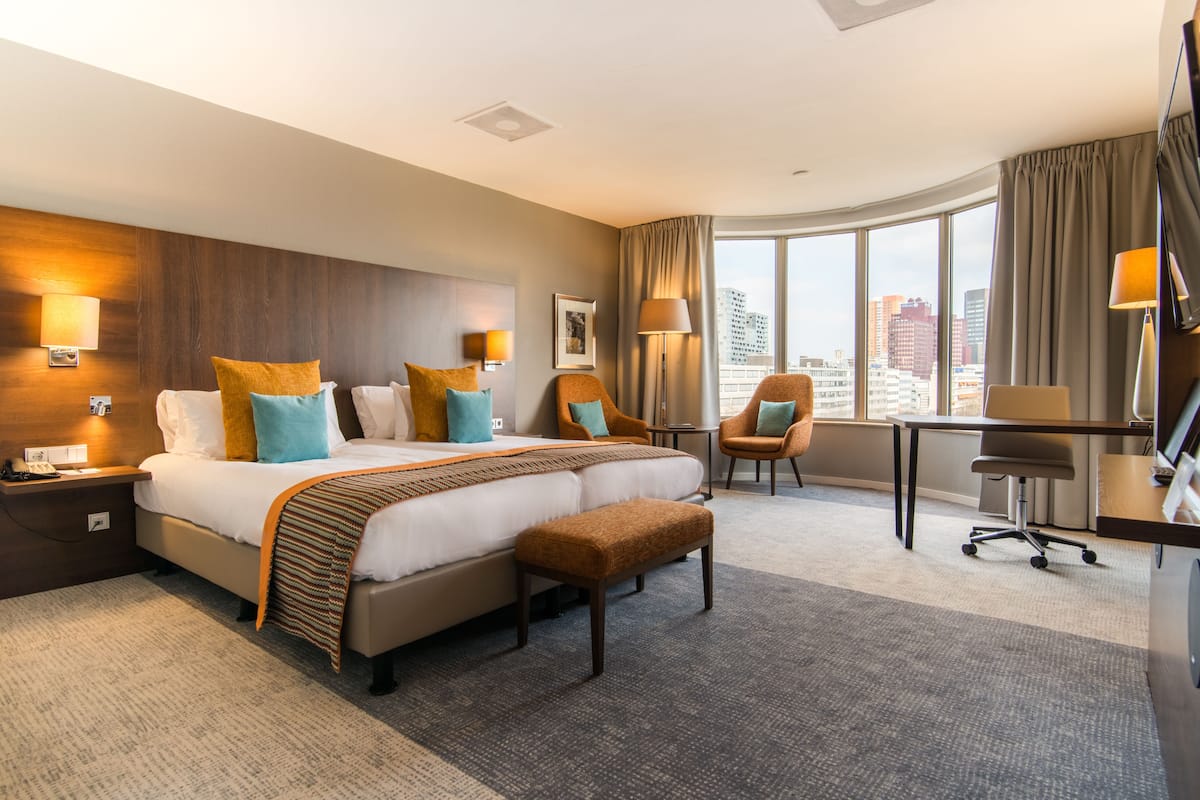 A hotel room with a large bed, two armchairs, a desk, and a view of the city.