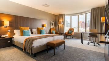 A hotel room with a large bed, two armchairs, a desk, and a view of the city.