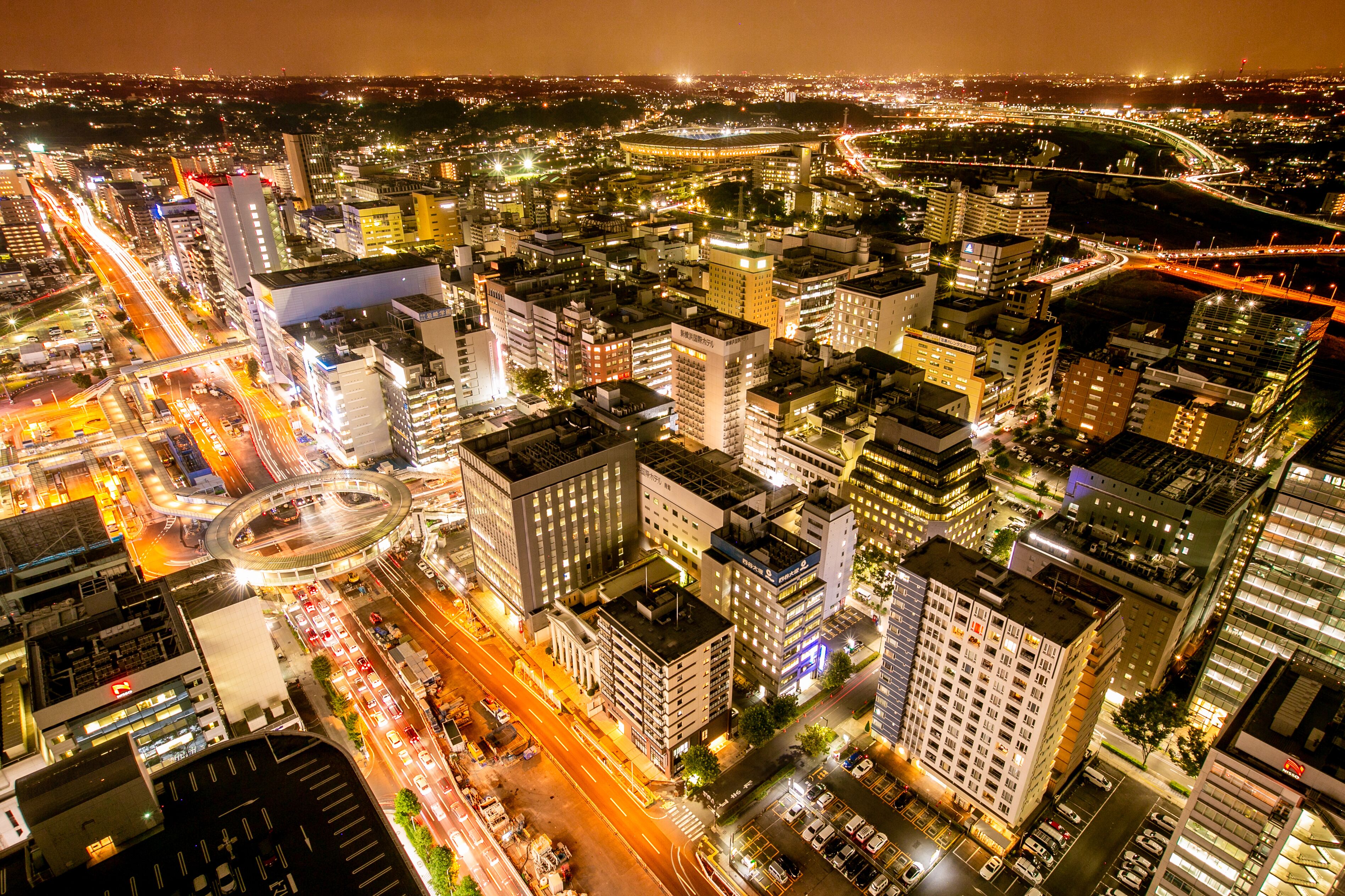 A nighttime cityscape with high-rise buildings, busy streets, and a prominent roundabout.