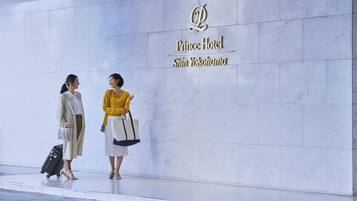 Two individuals standing in front of a hotel sign with a marble wall background.