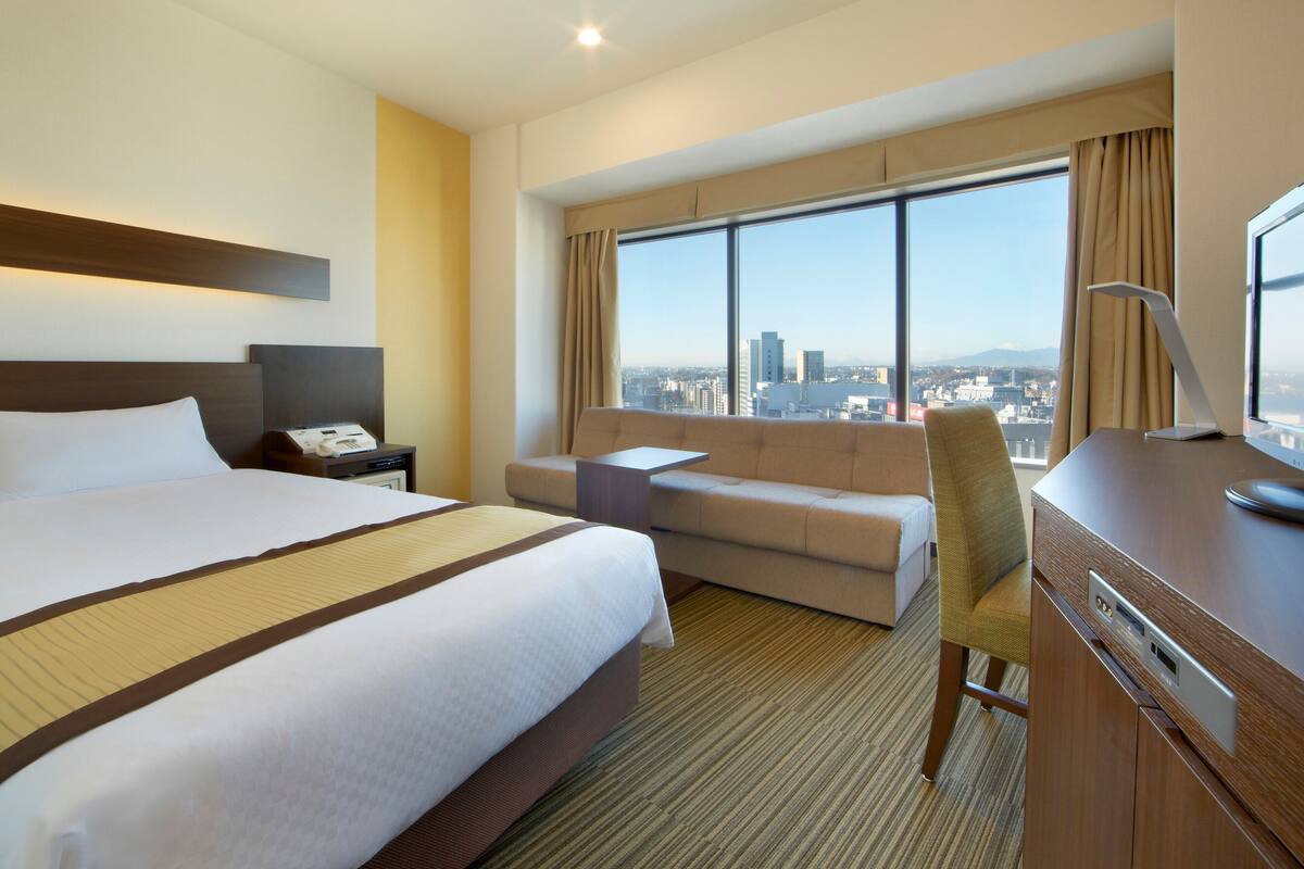 Ein Hotelzimmer mit einem großen Bett, einer Couch, einem Schreibtisch mit Computer und Blick auf die Stadt.