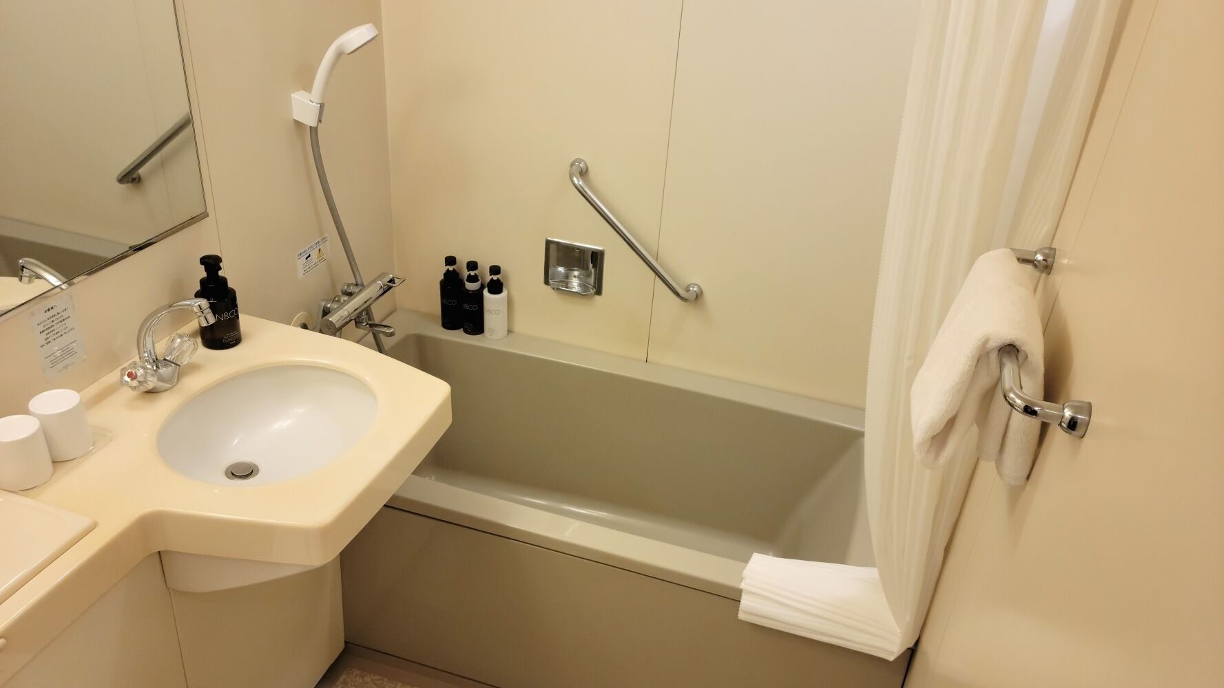 A bathroom with a sink, mirror, shower, and towel rack.