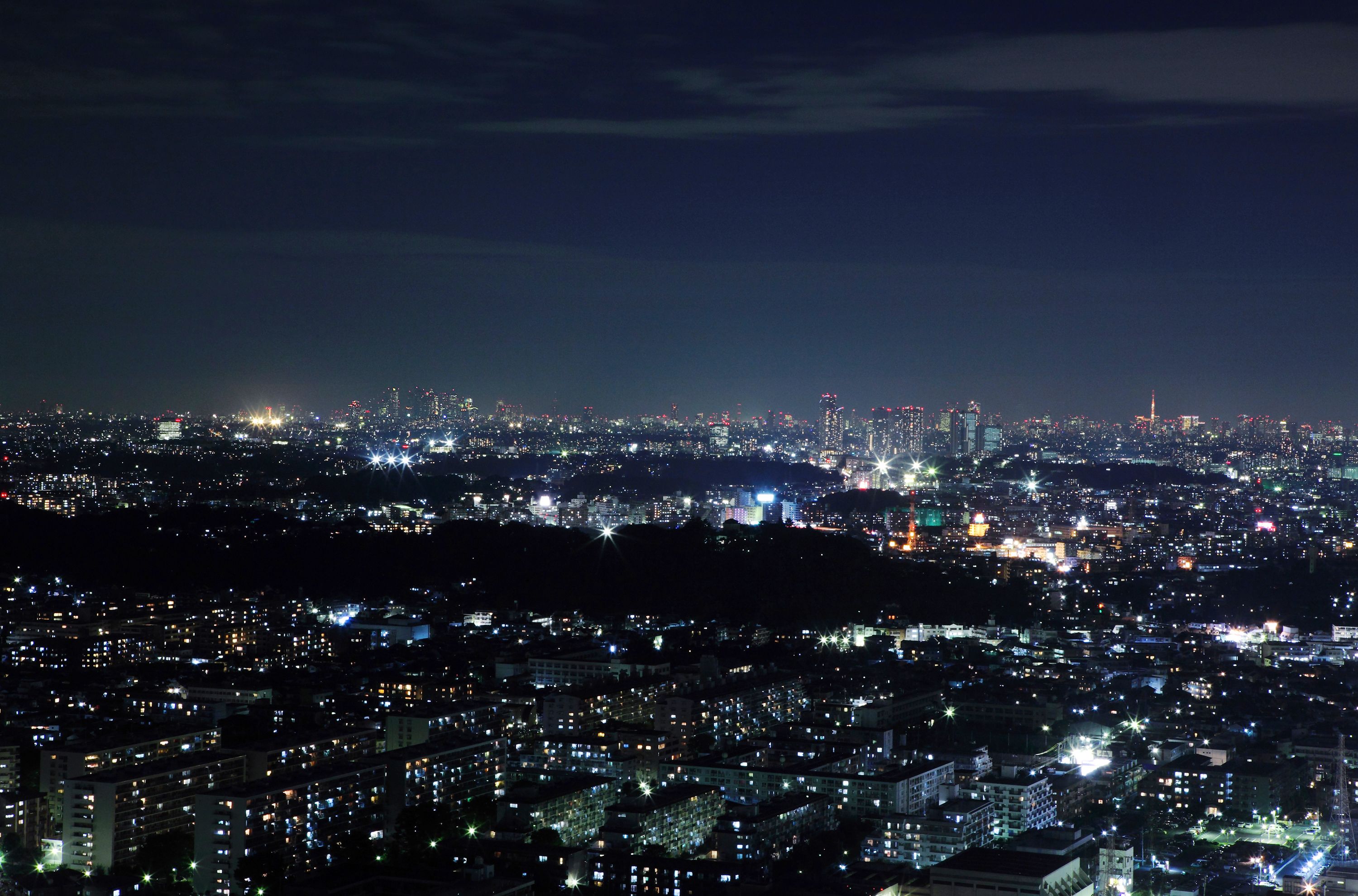 A nighttime cityscape with dense urban lighting and distant high-rise buildings.