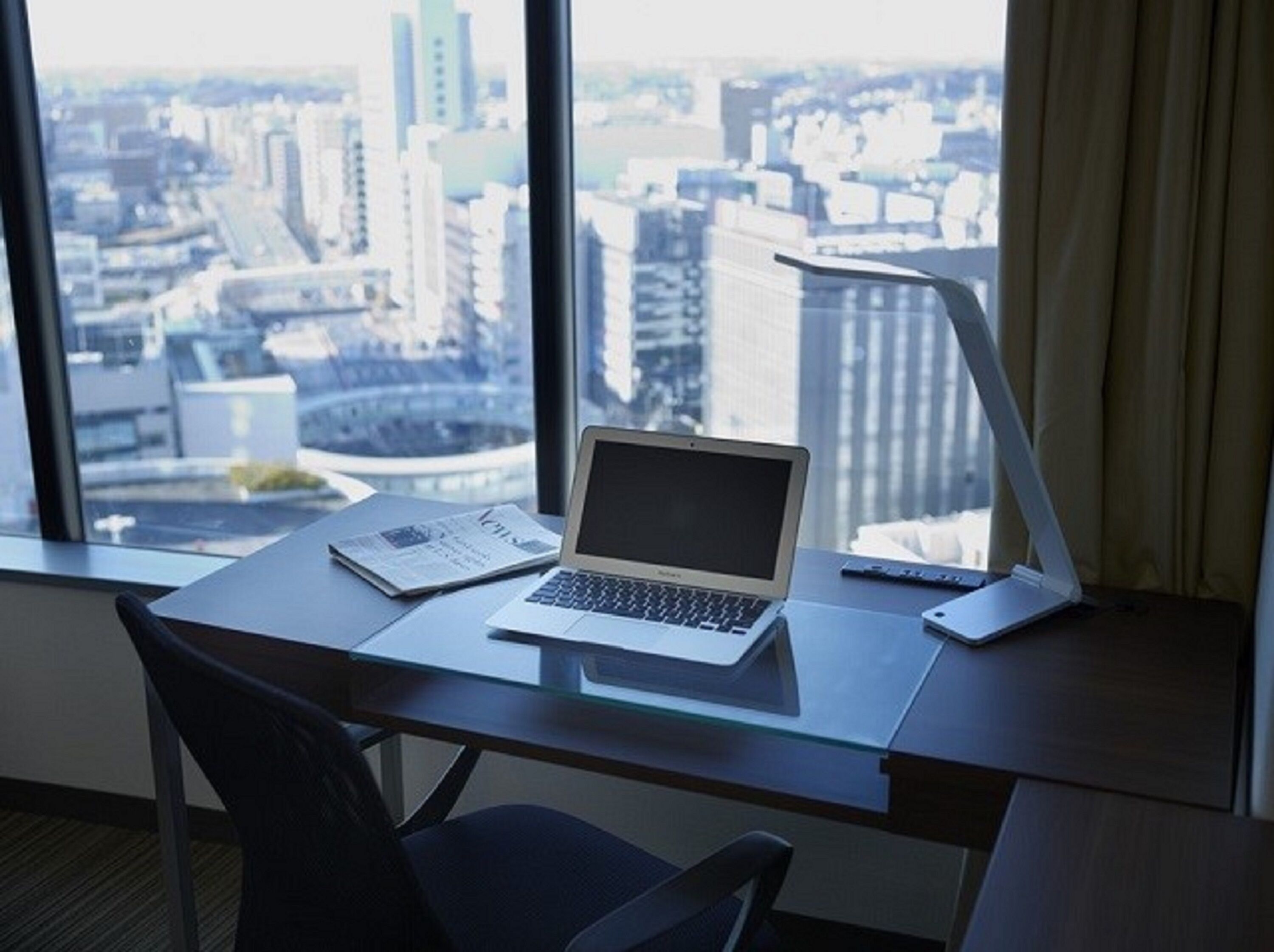 A modern office desk with a laptop and a tablet, positioned near a window with a city view.