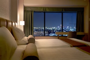 Quarto de hotel com uma grande janela que oferece vista para a cidade à noite.