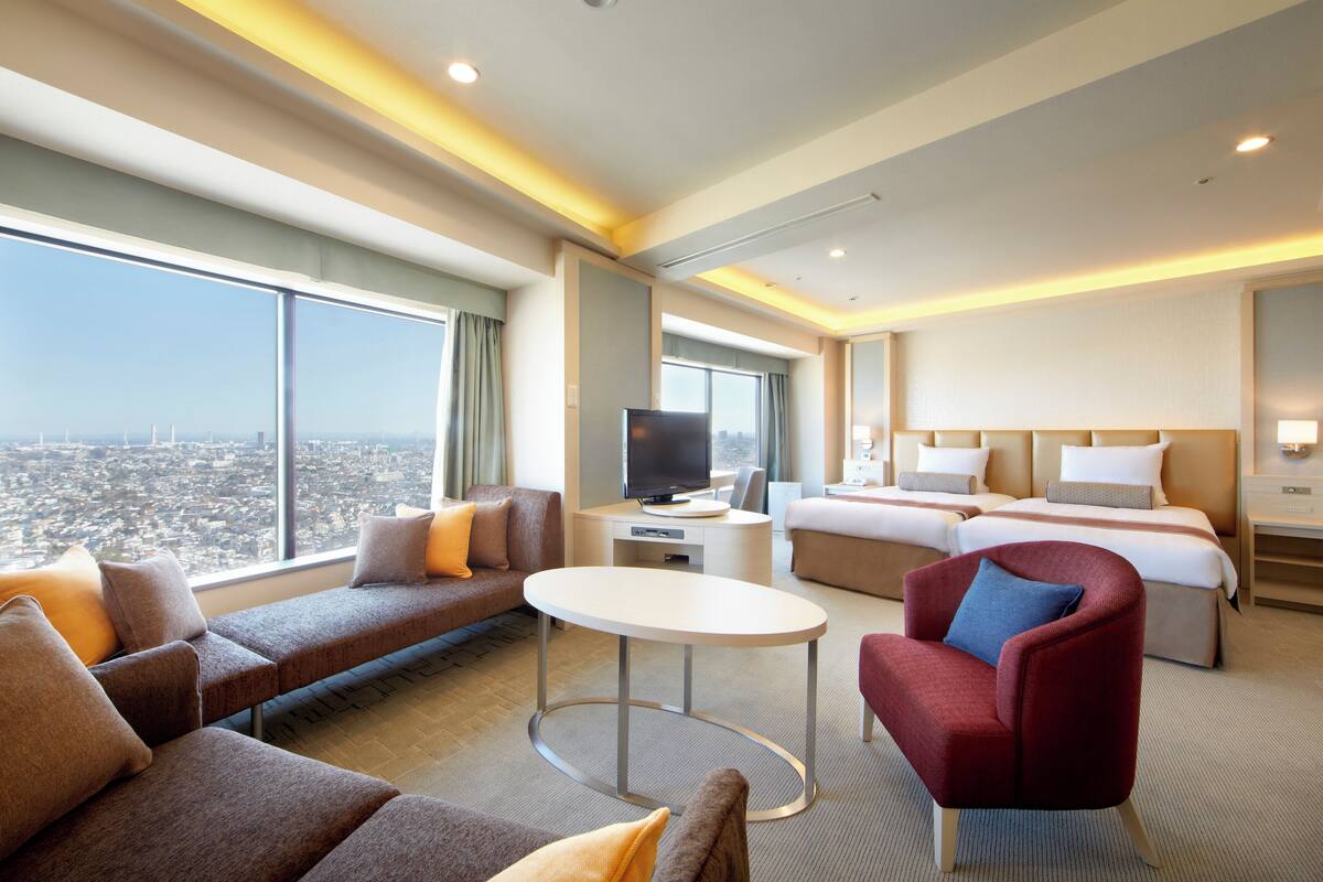 Ein Hotelzimmer mit Blick auf die Stadt, einem großen Bett, einem Schreibtisch mit Fernseher und einer Sitzecke mit Sofas und einem roten Sessel.