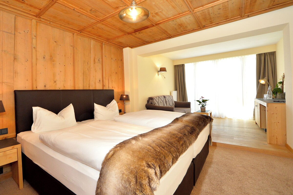 Habitación de hotel con una cama grande, paredes de madera, un escritorio y vistas al exterior.