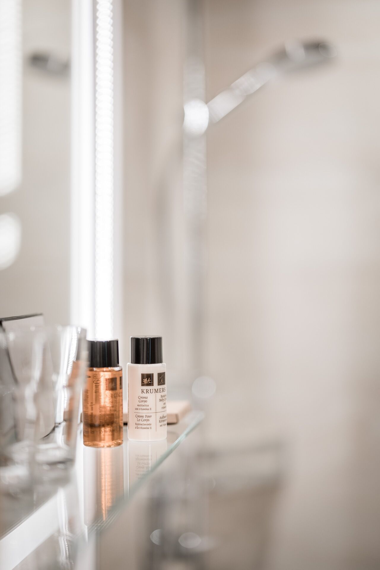 A bathroom with a glass shelf holding two skincare products and a glass container.