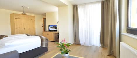 A hotel room with a bed, a small table with a plant, a television, and a wooden wardrobe.