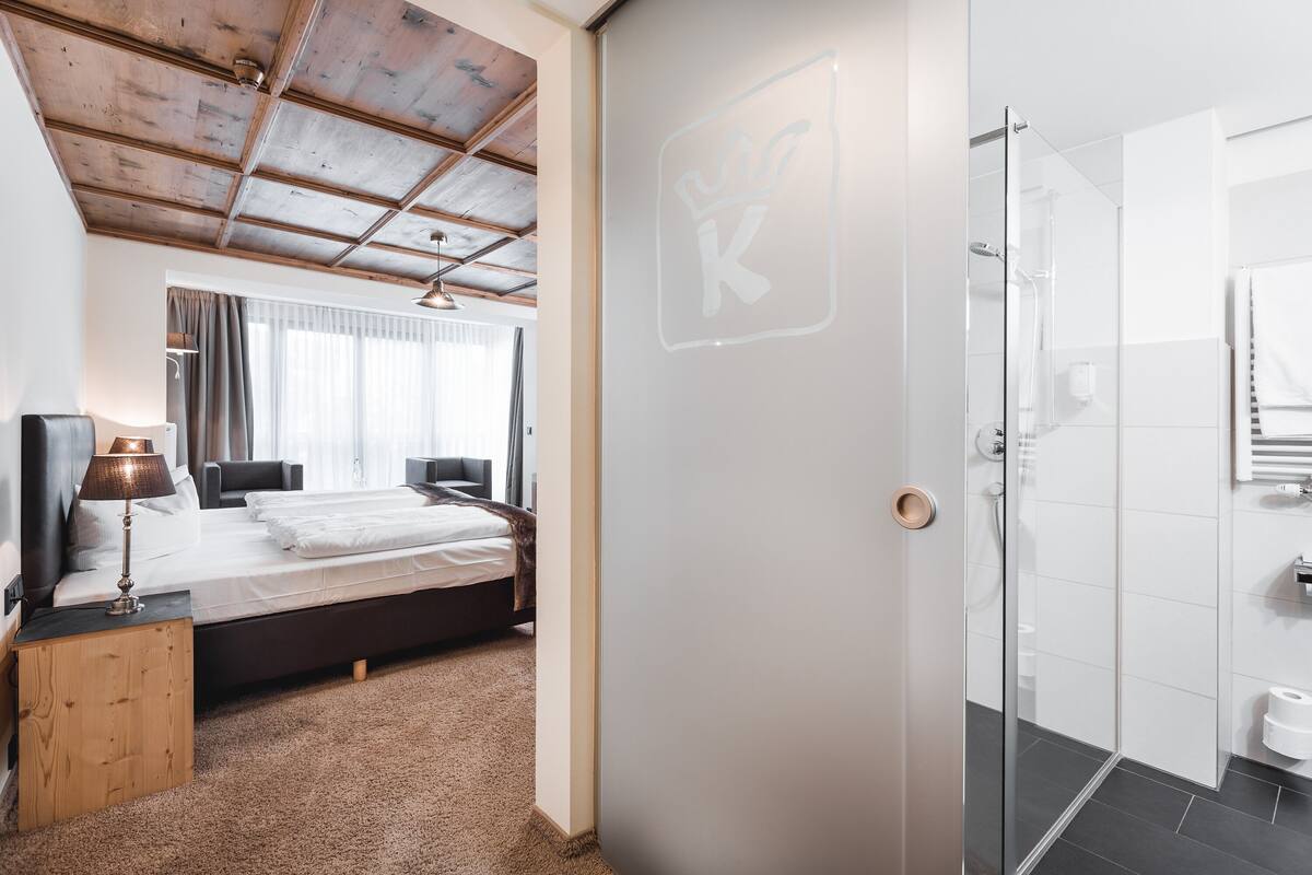 A bedroom with a bed, bedside table, lamp, and a large window with curtains.