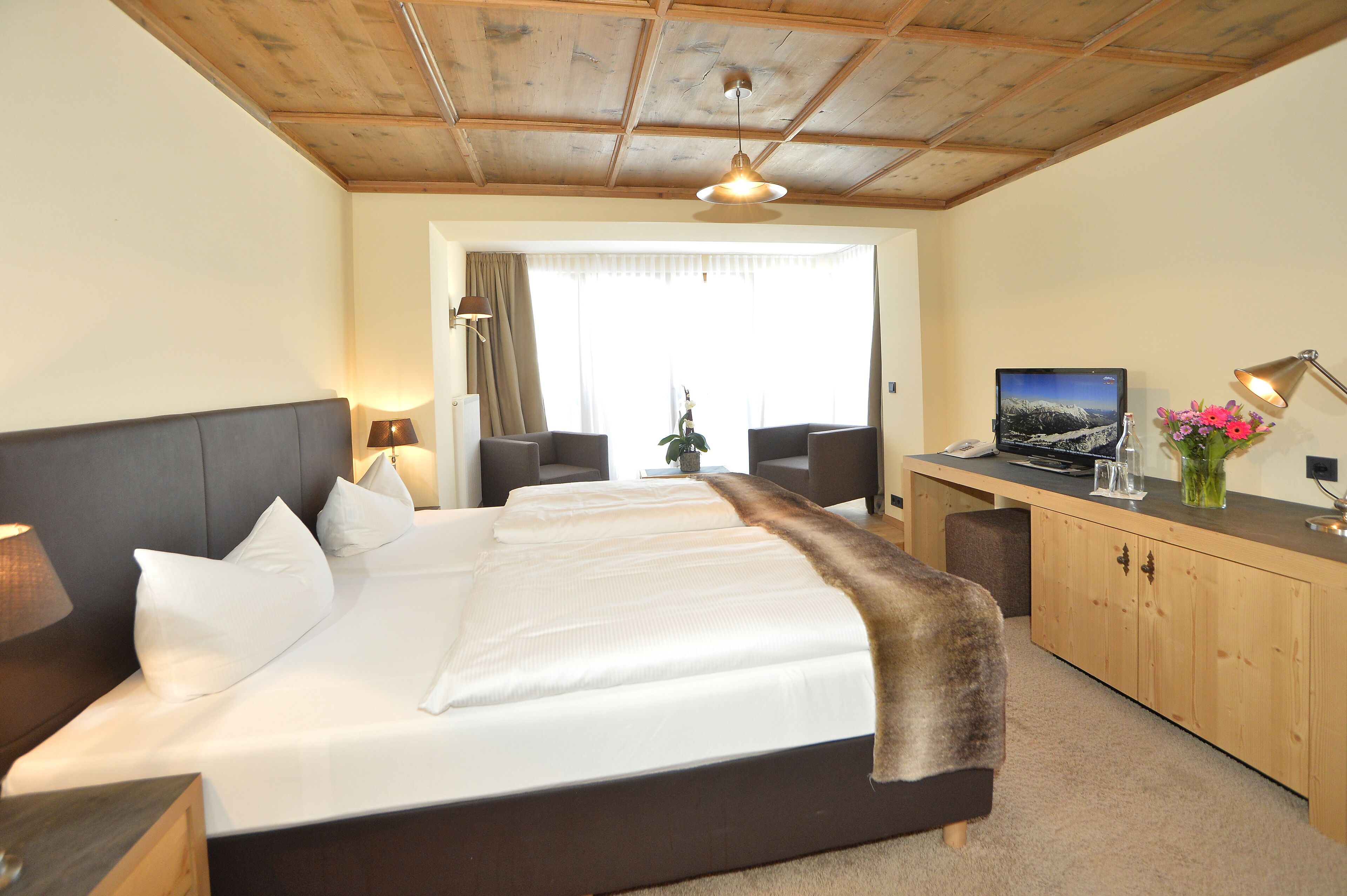 A hotel room with a large bed, a desk with a computer, a TV, and a window with curtains.