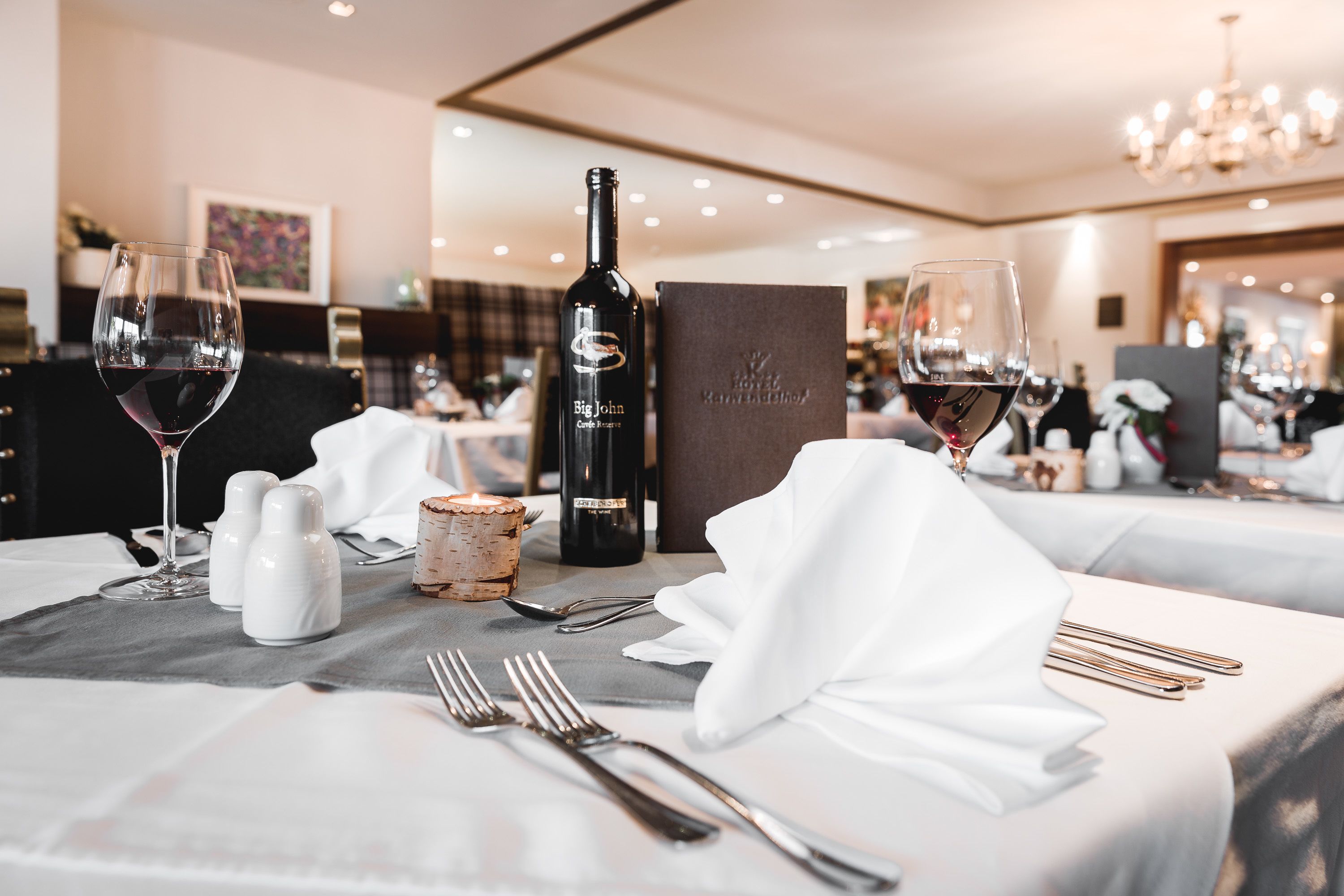 A well-set dining table with wine glasses, a bottle of wine, salt and pepper shakers, and a menu box.
