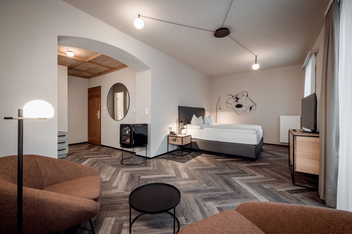 A modern hotel room with a bed, a desk, a TV, and a seating area.