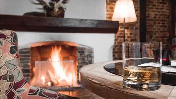 Un vaso de whisky sobre una mesa de madera, con una chimenea al fondo.