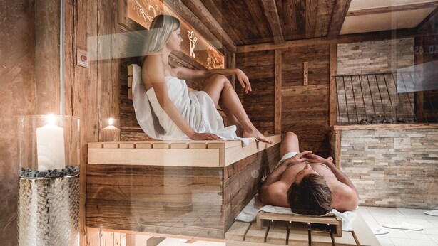 Una habitación tipo cabaña de madera con sauna, pared de piedra y banco de madera.