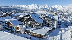Un resort cubierto de nieve con edificios de estilo chalete, un telesilla y un paisaje montañoso de fondo.